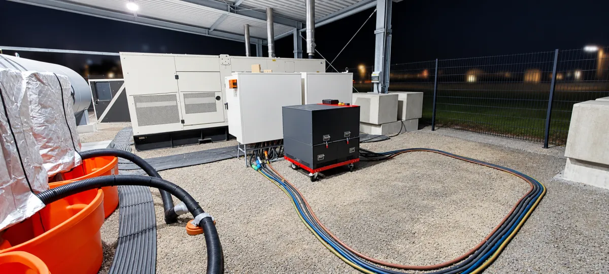 Lastbank mit rotem Fahrgestell bei Nacht vor Aggregat und Schaltschränken, Lastkabel im Bogen verlegt